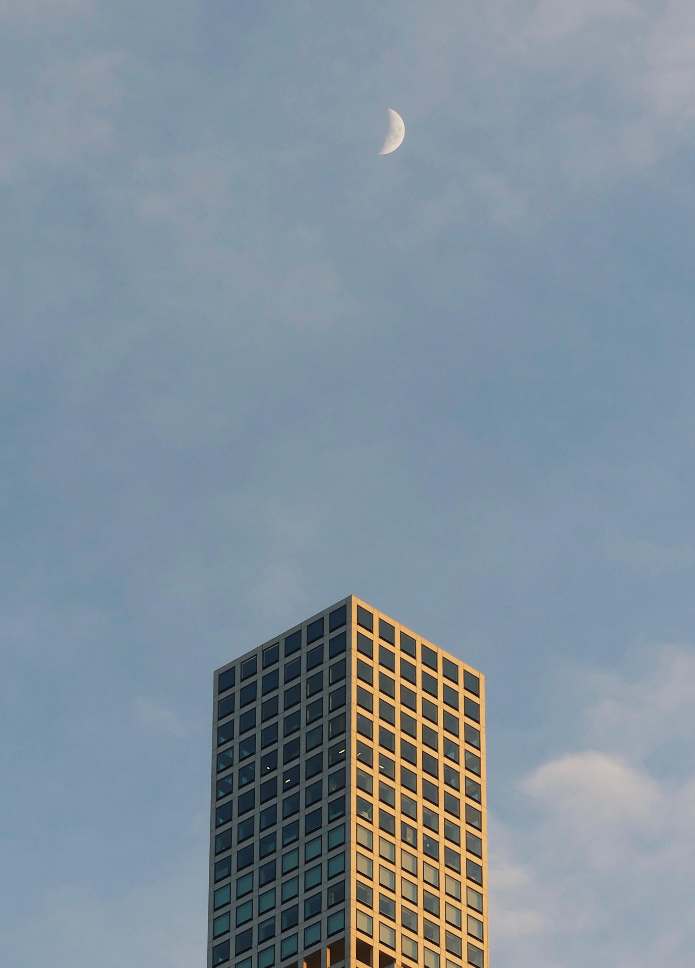 Skyscraper at sunset with a crescent moon above.