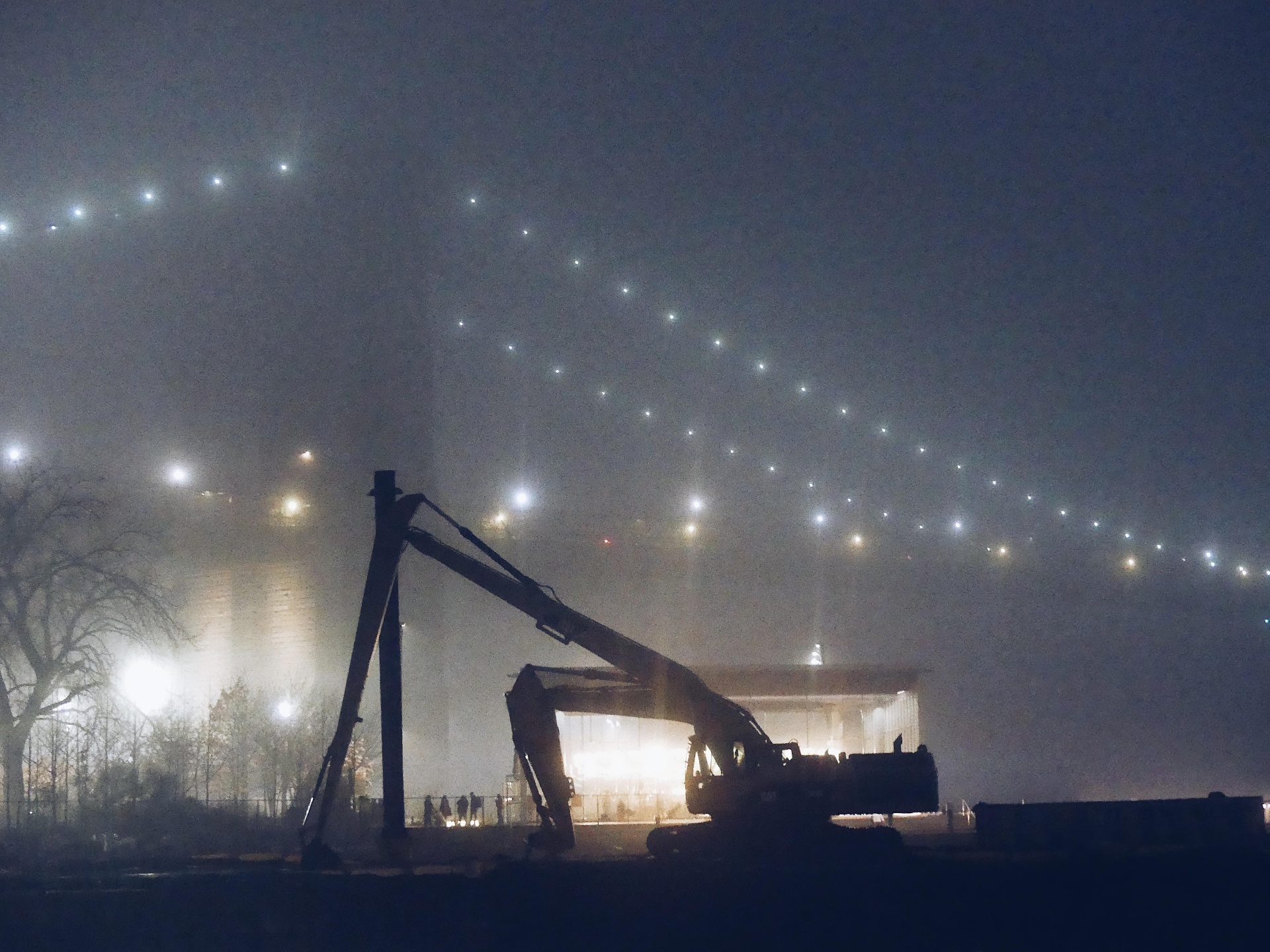 Excavator silhouetted against a foggy night sky of scattered lights.