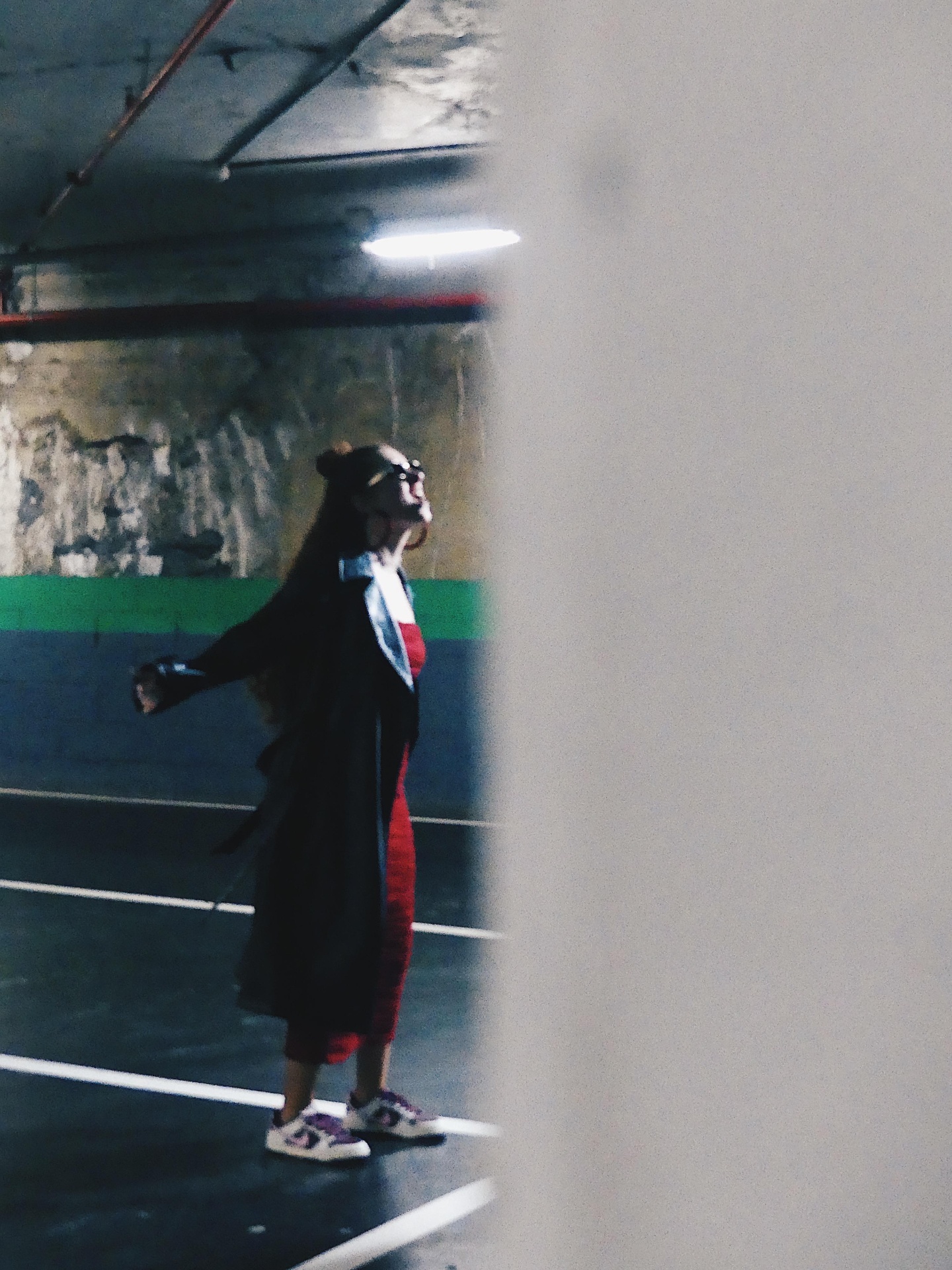 Woman in red dress and black coat laughing in a parking garage with painted walls.