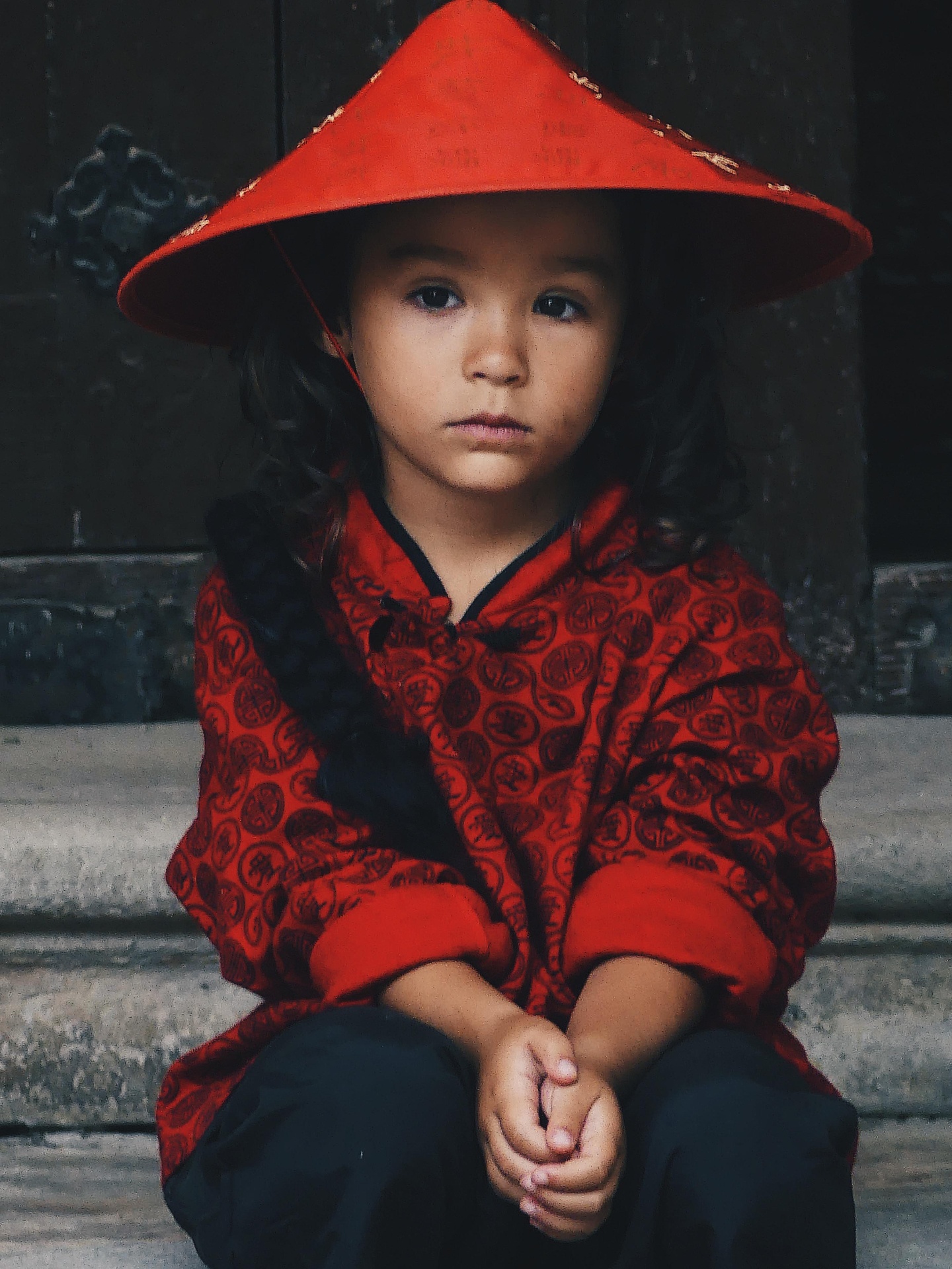Child wearing a red conical hat and traditional clothing.