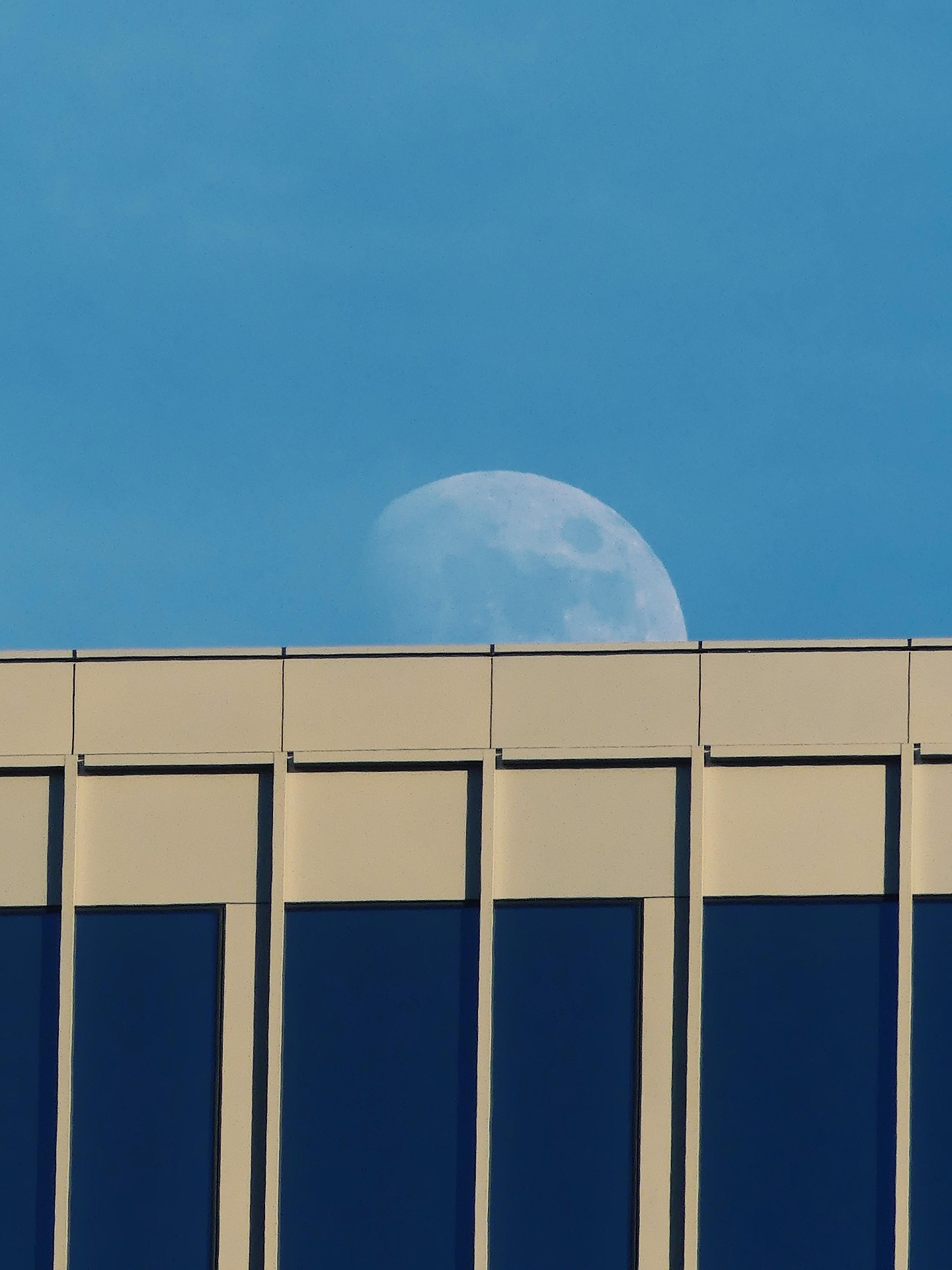 Full moon rising behind the cornice of a modern office building.