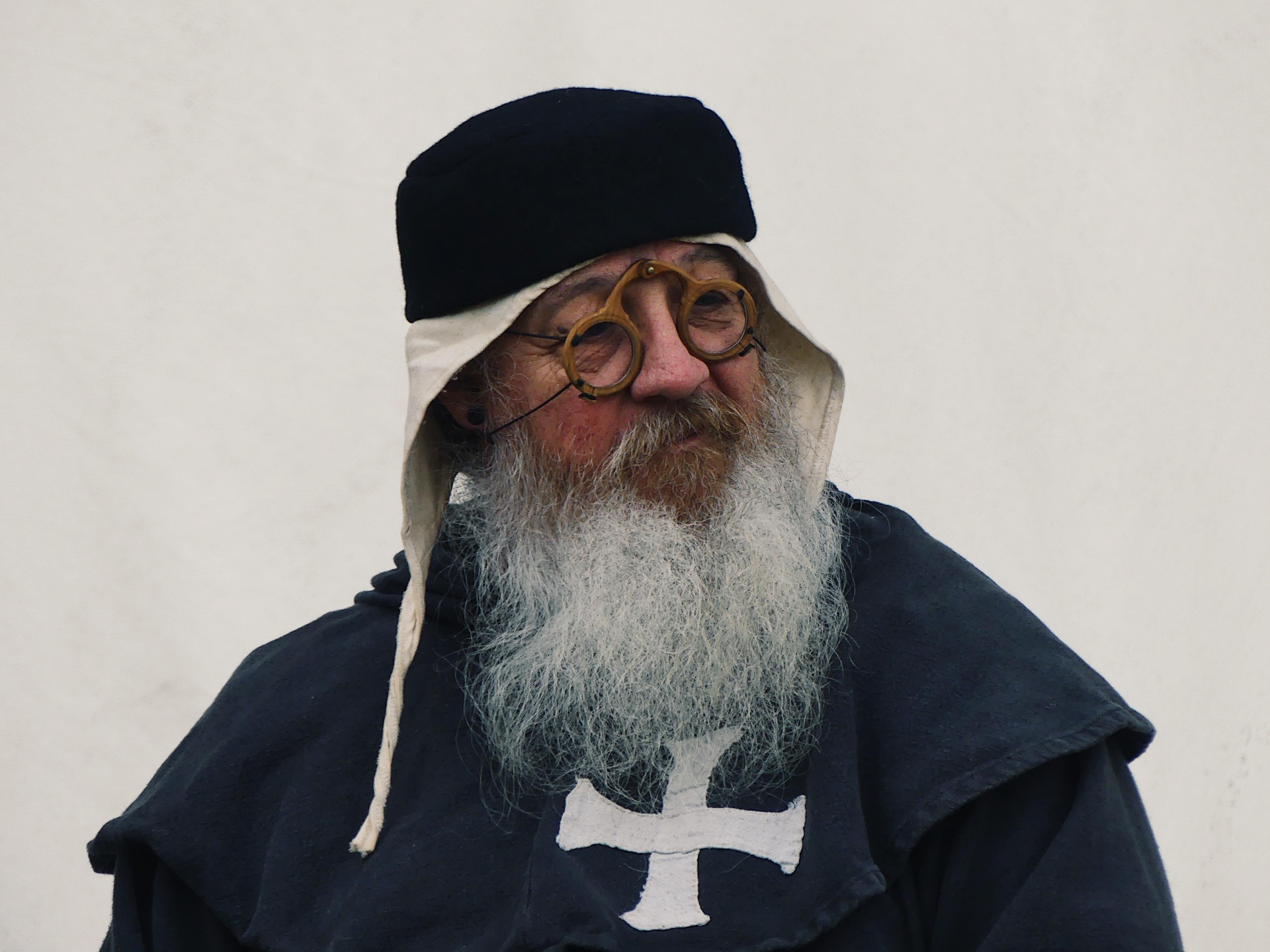 Portrait of a bearded man in historical costume with round glasses and a cross emblem.