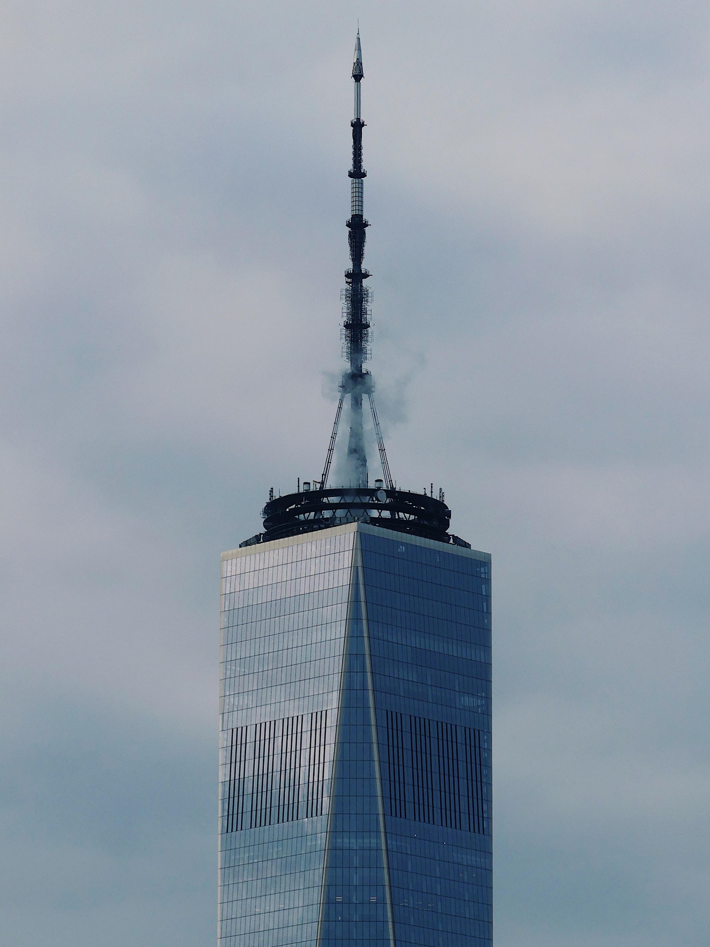 Top of One World Trade Center against cloudy sky.